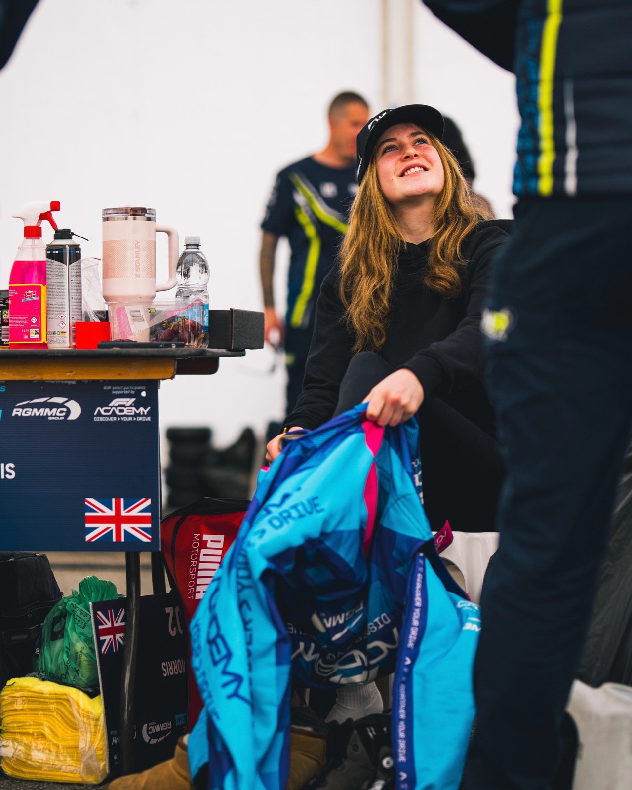 Eva smiling up from her seat in the paddock beside the F1 Academy Discover Your Drive board