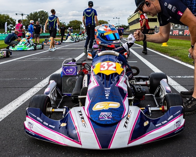 Eva's navy, pink and white #32 kart on the grid at Kartmasters, covered in partner stickers, as a team member gives her a fist bump